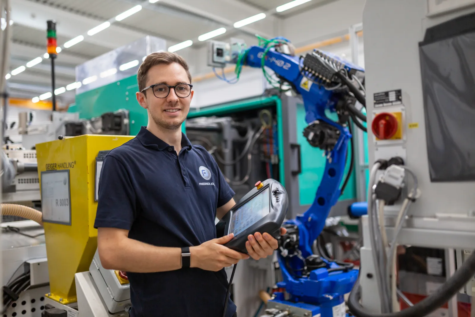 Junger Techniker mit Bediengerät an Spritzguss-Zelle und Roboter